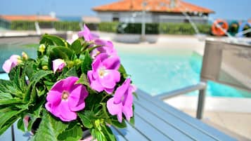 Zona de piscina amb un arranjament floral, una piscina i un edifici amb teulada vermella al fons.