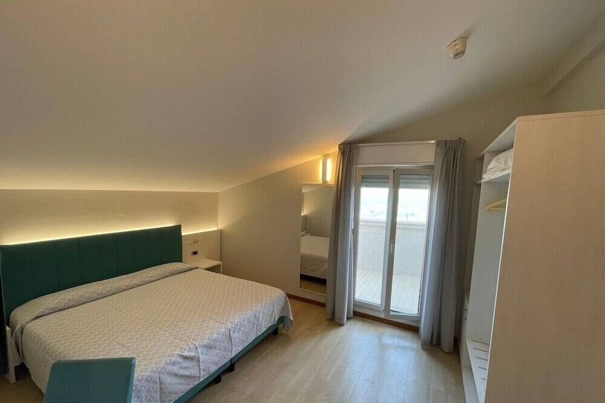 Una habitación de hotel con cama, escritorio, silla, armario y balcón con cortinas.