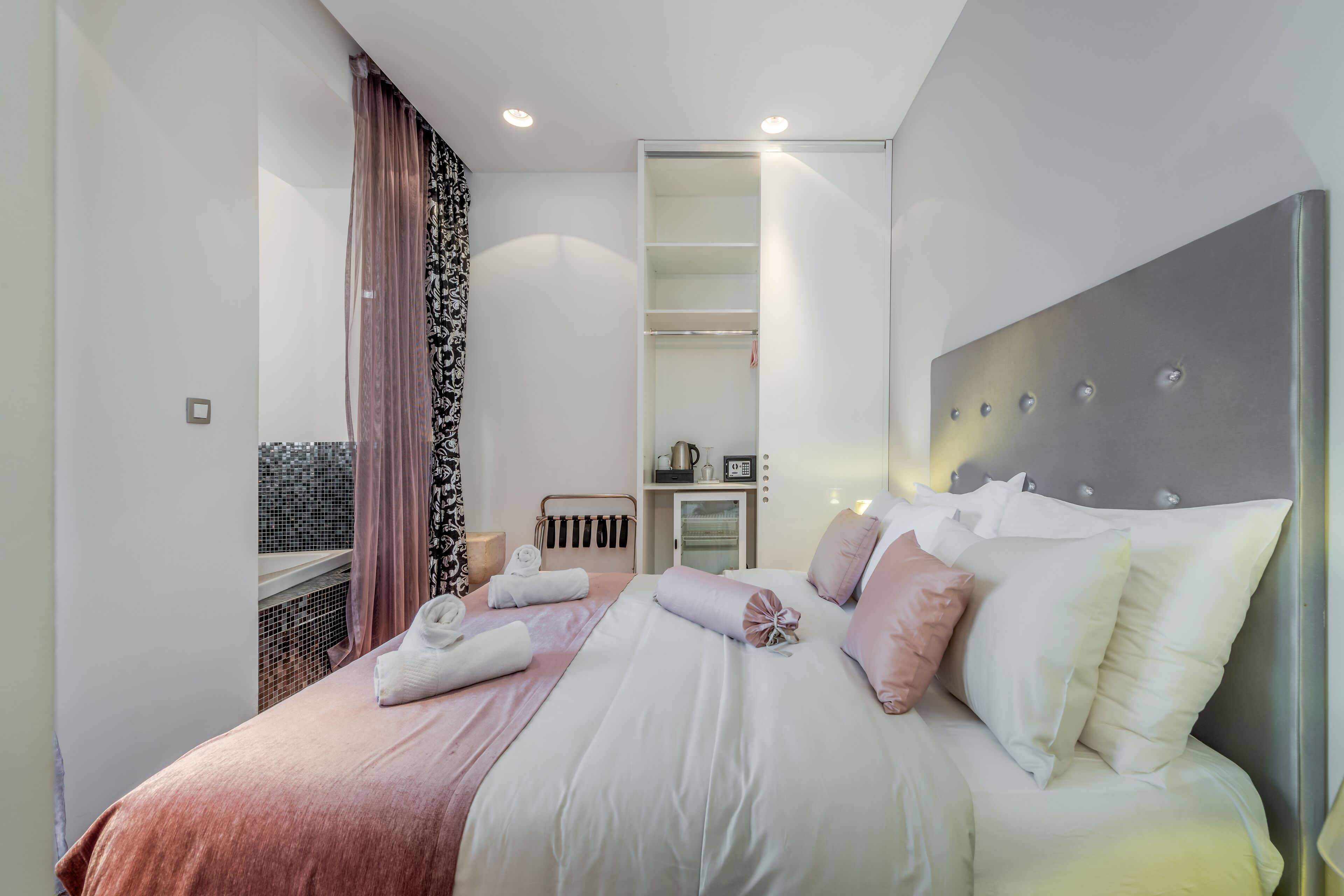 A modern hotel room with a large bed, a walk-in closet, and a view through a window.