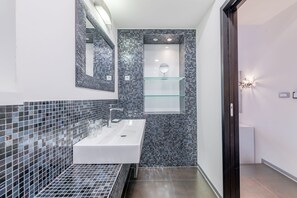 Un bany modern amb un lavabo blanc, una prestatgeria de vidre i un mirall.