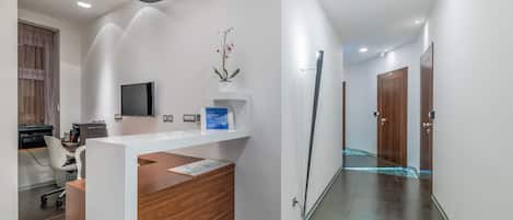 A modern reception area with a wooden reception desk, a flat-screen TV, and a vase with flowers.