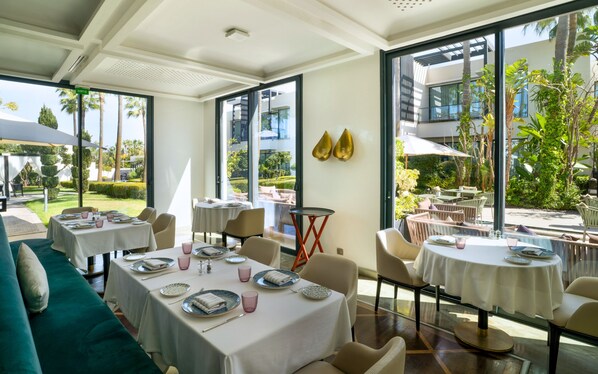 Un comedor interior con mesas dispuestas para los huéspedes, amplias ventanas que ofrecen vistas al jardín y un diseño arquitectónico moderno.