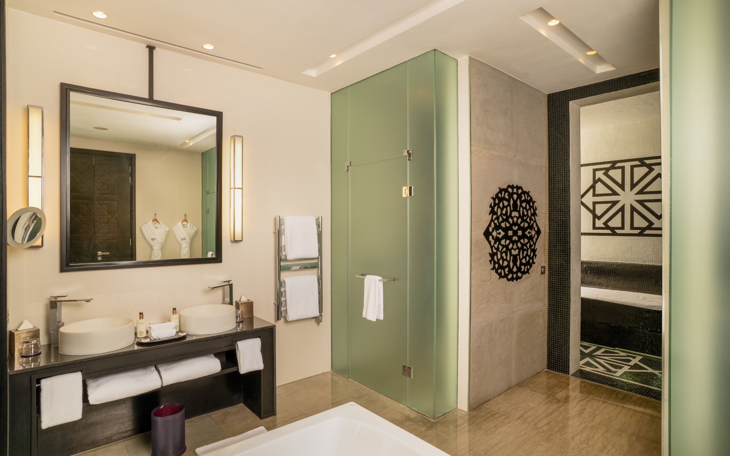A modern bathroom with a large mirror, two sinks, a bathtub, and a shower area.