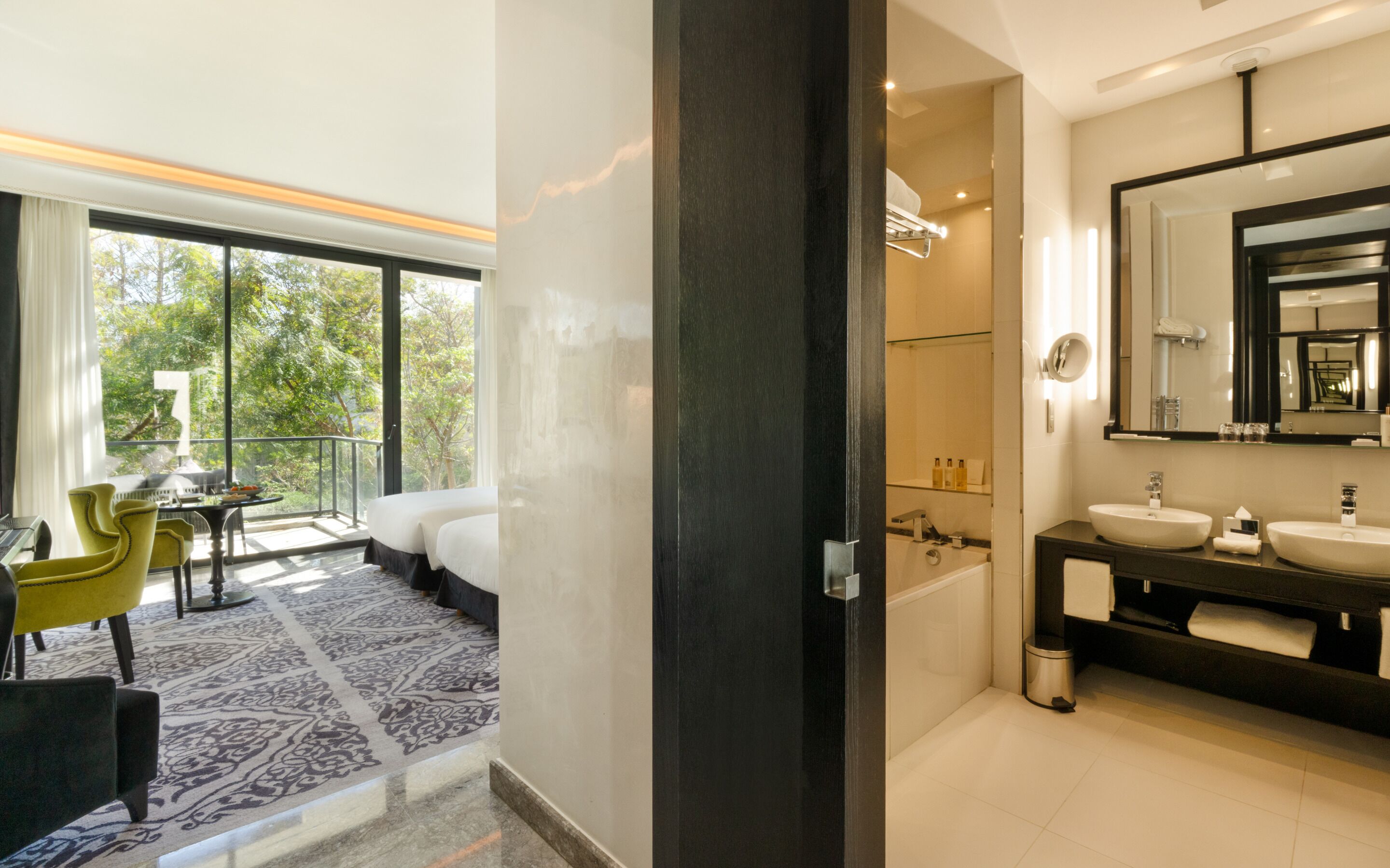Une chambre d’hôtel moderne avec balcon, une salle de bain dotée d’un grand miroir et un tapis à motifs.