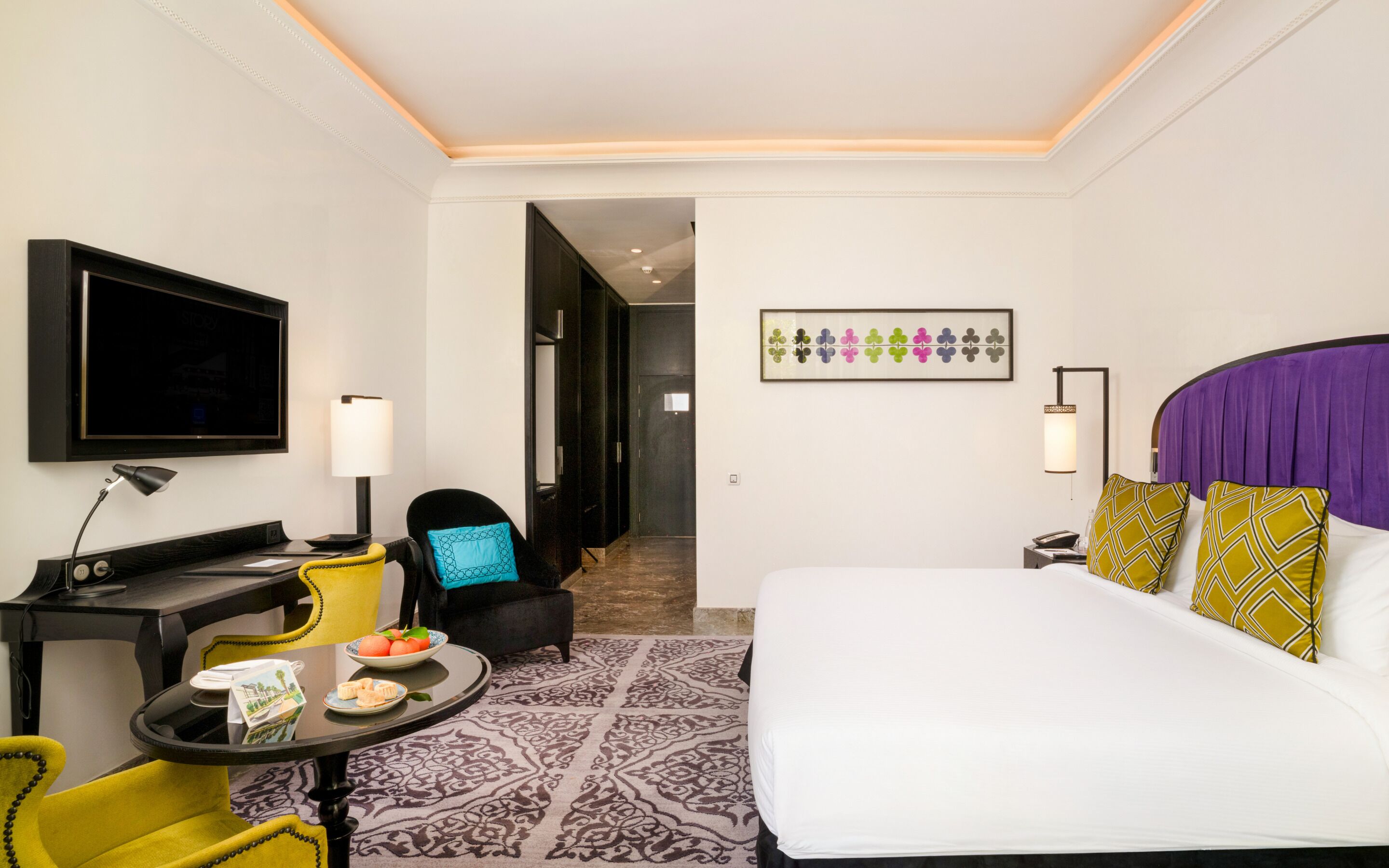 A hotel room with a bed, a desk with a lamp, a chair, a television, and a framed picture on the wall.