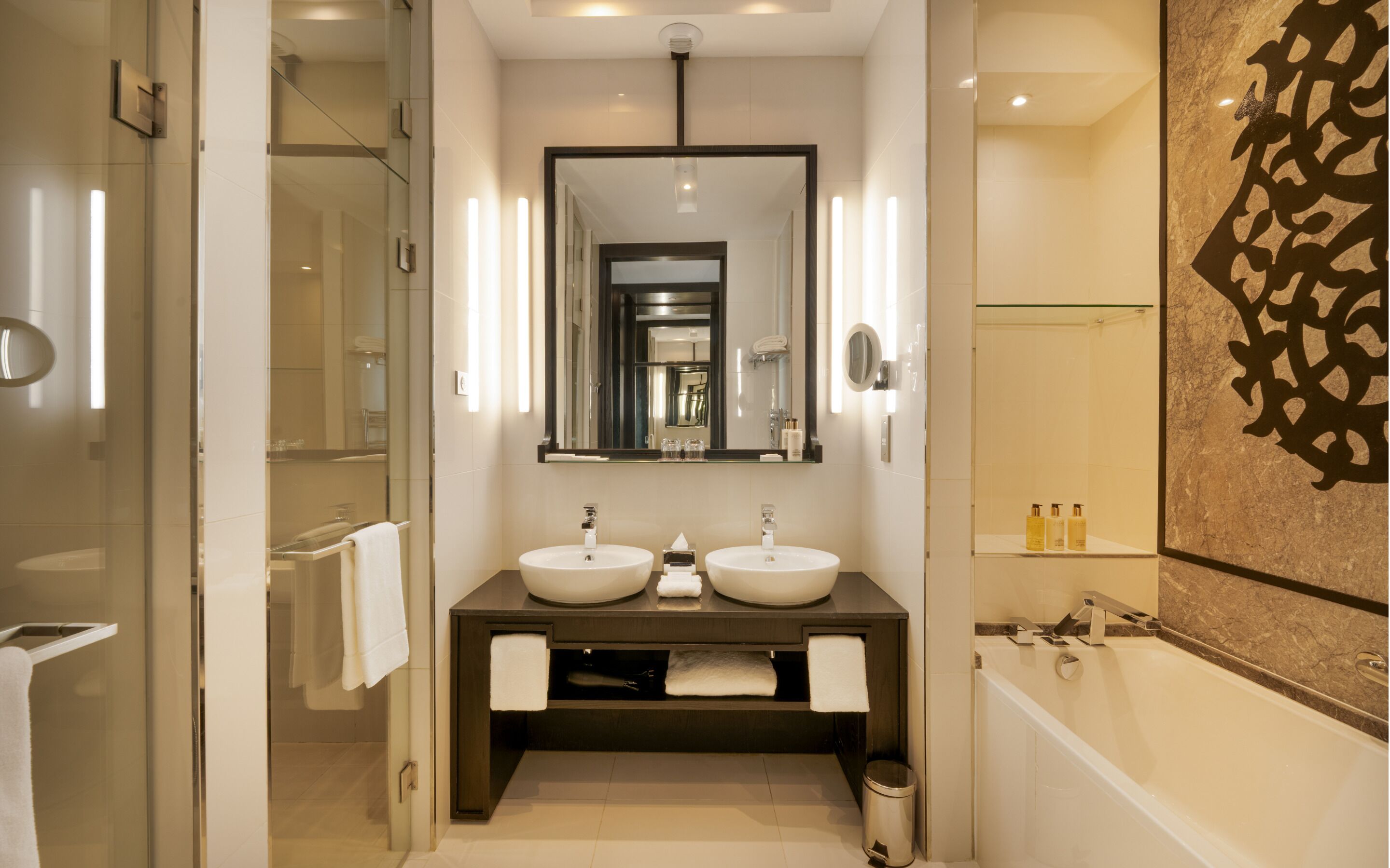 Une salle de bain moderne avec deux lavabos, un grand miroir et un espace douche.