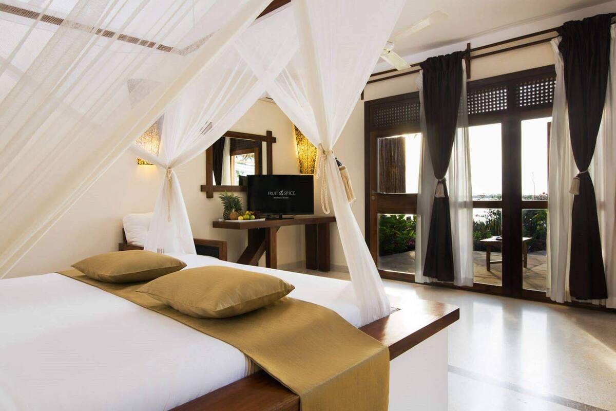 A bedroom with a bed, a TV, a desk, and a view of the outdoors.