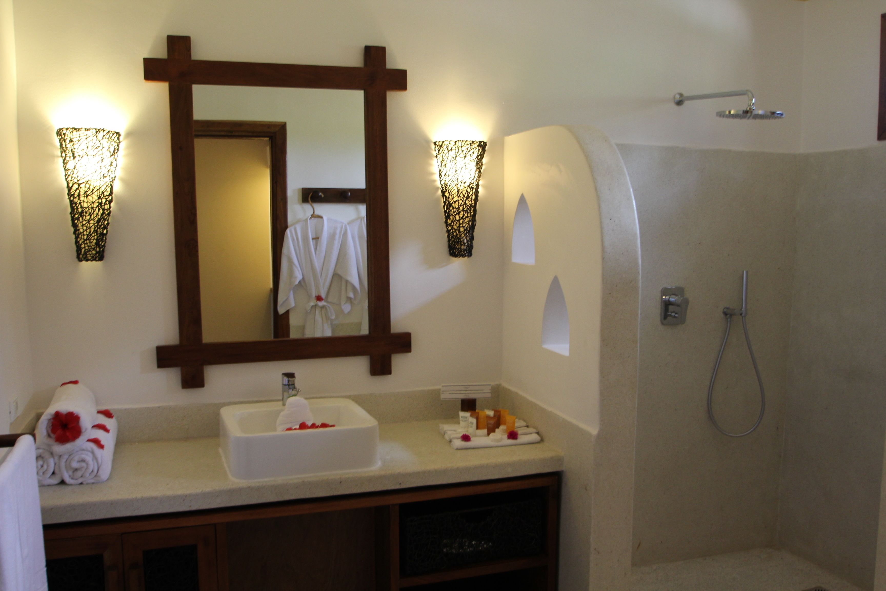A bathroom with a sink, mirror, towel rack, shower, and wall sconces.
