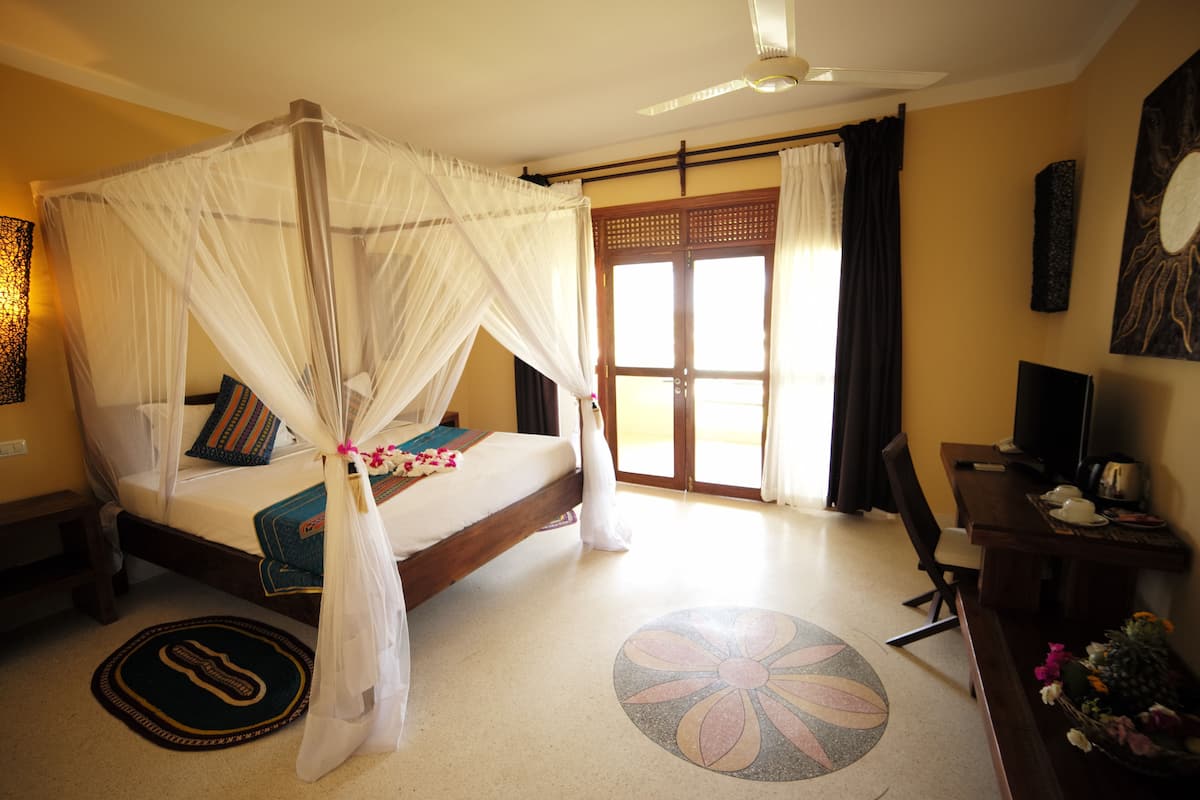 A room with a bed, a desk, a television, and a large window with curtains.