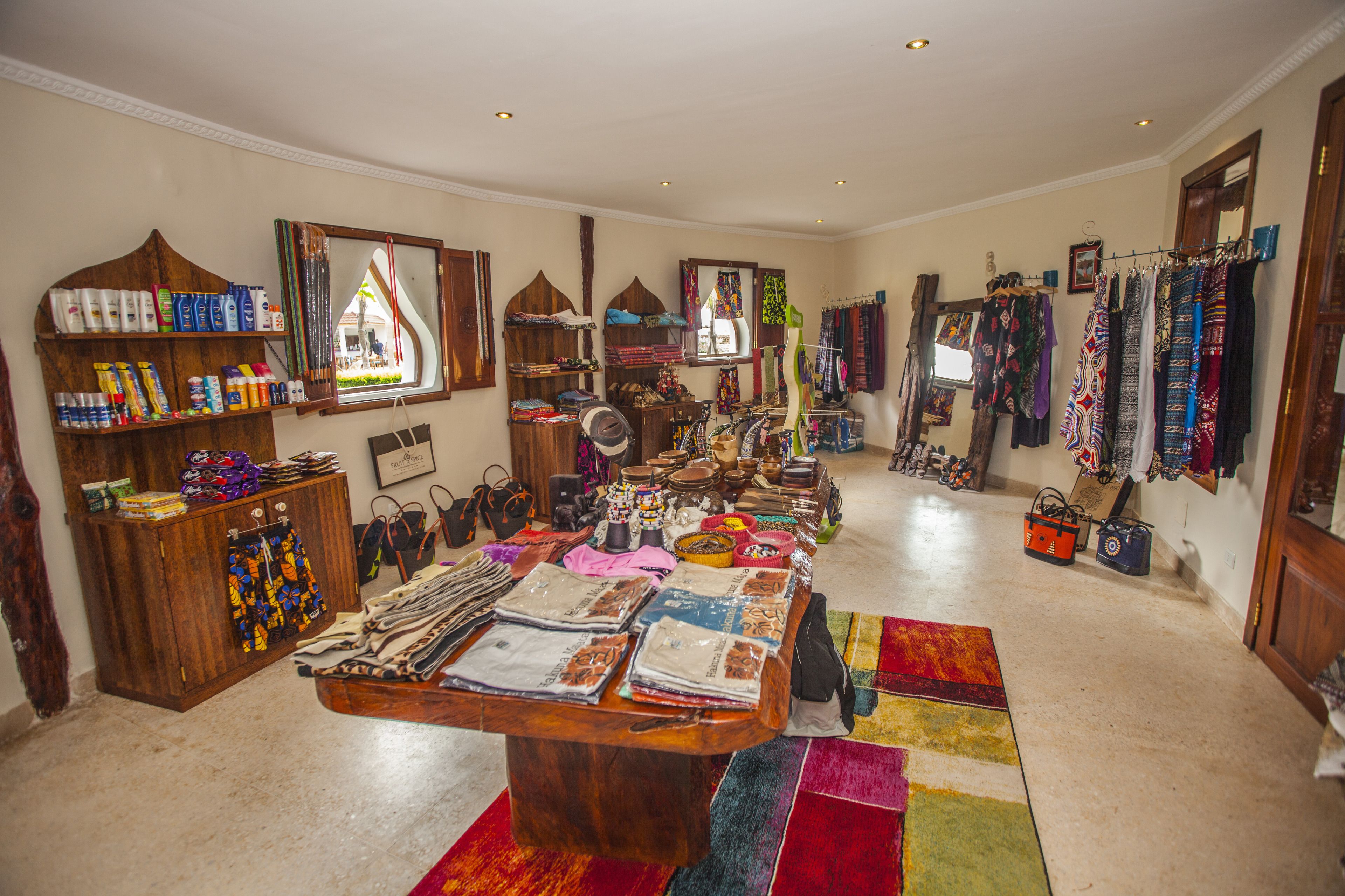 Une pièce comprenant une longue table où sont exposés divers tissus et textiles, des étagères remplies de produits de nettoyage et un miroir qui reflète la pièce.