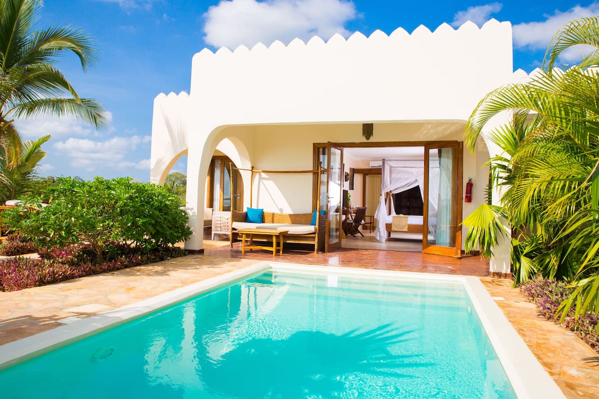 A pool area with a white building, a lounge chair, and a small table.
