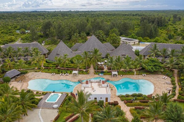Un resort con varias cabañas de techo de paja, una piscina central y palmeras alrededor.