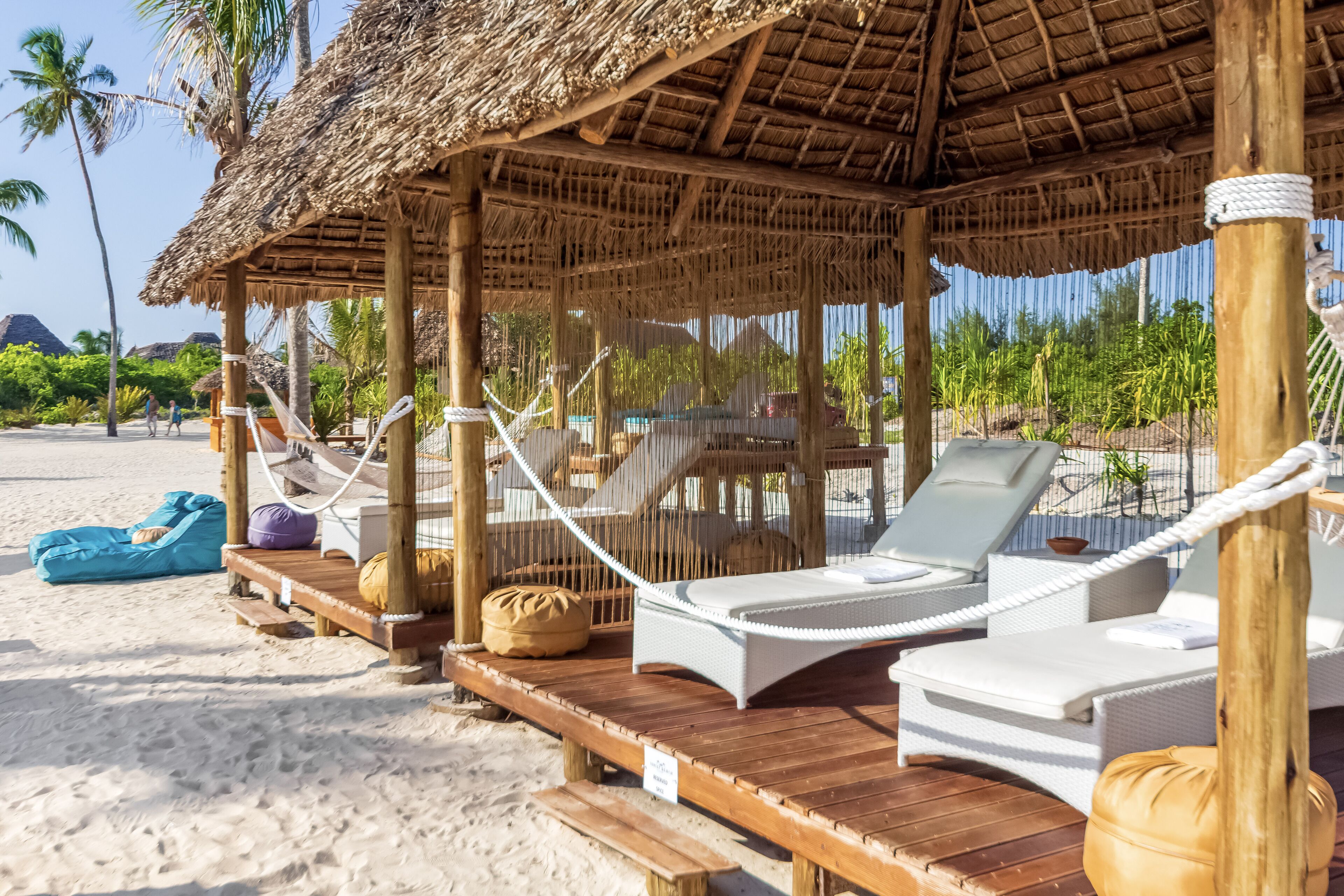 Un petit chalet au bord de la plage, avec un plancher en bois et des chaises longues blanches.