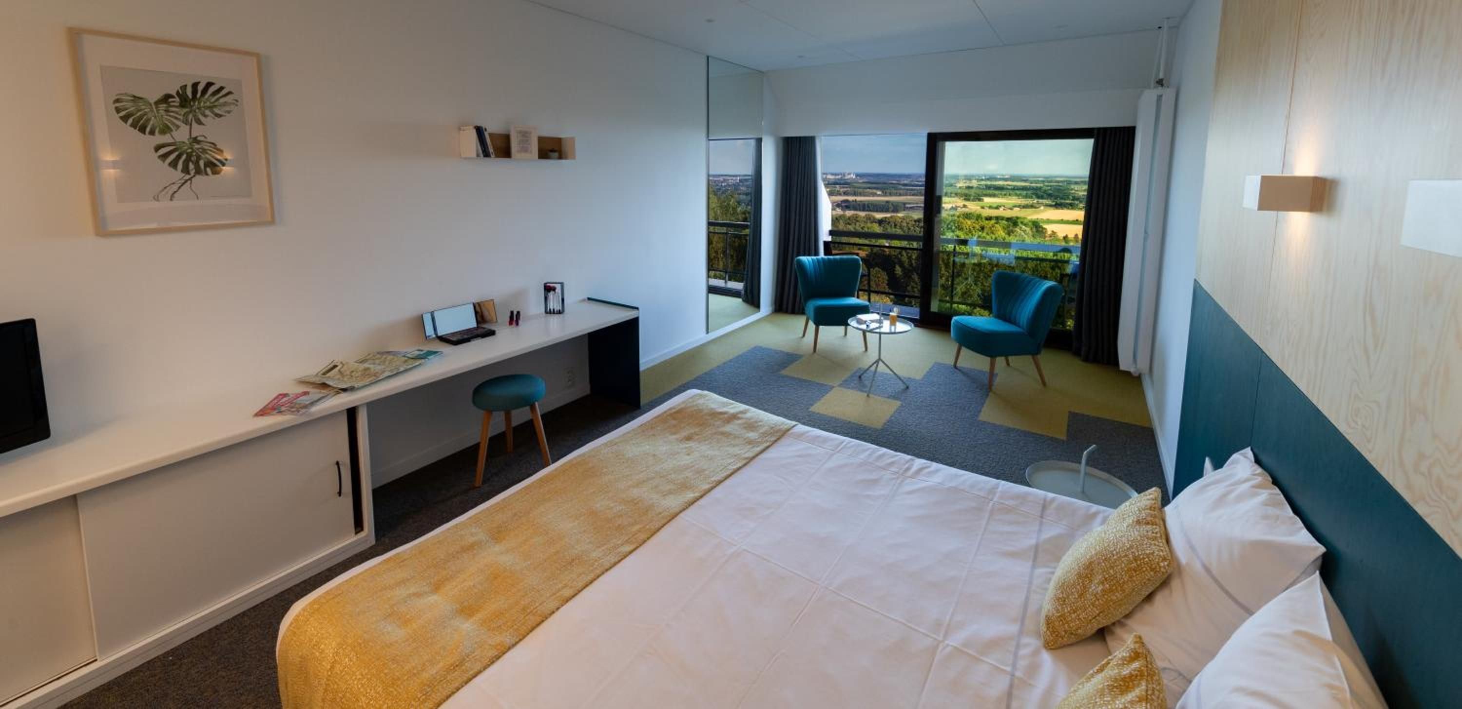 Een hotelkamer met een bed, bureau, stoel en een balkon met uitzicht.