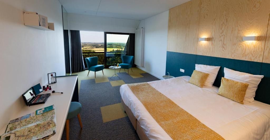 Una habitación de hotel con una cama grande, un escritorio con una computadora portátil, una silla y vistas al campo a través de un ventanal amplio.