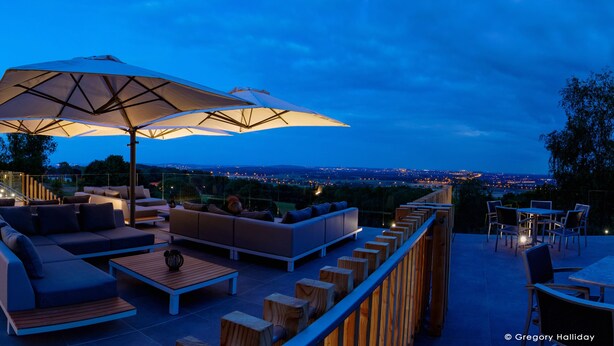 An outdoor seating area with modern furniture and umbrellas, overlooking a cityscape at dusk. - Le Floreal Panoramique (Tournai)