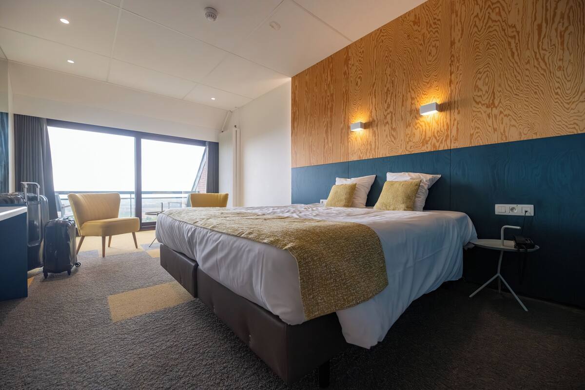 A hotel room with a large bed, a desk, a chair, and a view of the sea.