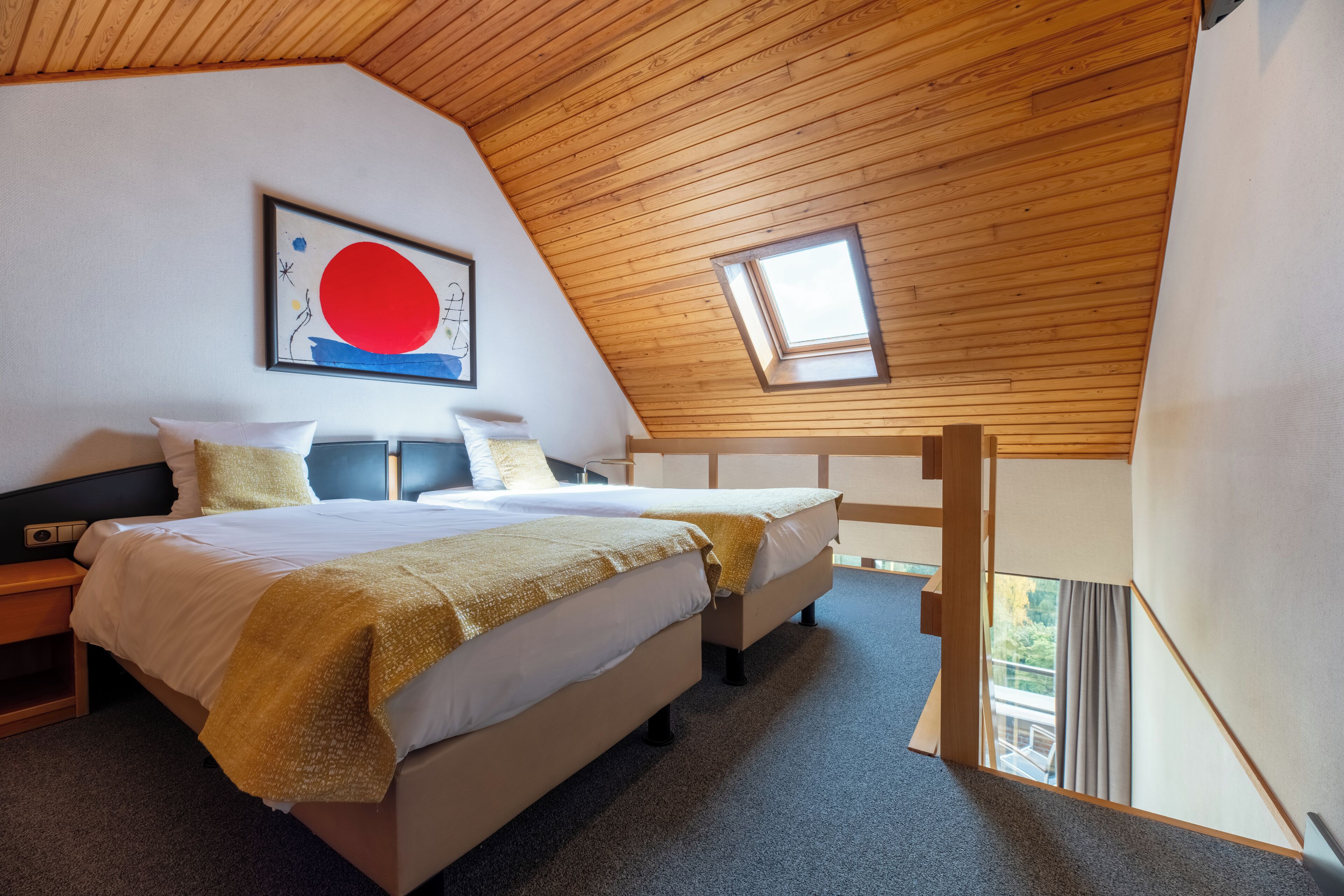 Un dormitorio con dos camas, techo de madera, tragaluz y una obra de arte enmarcada en la pared.