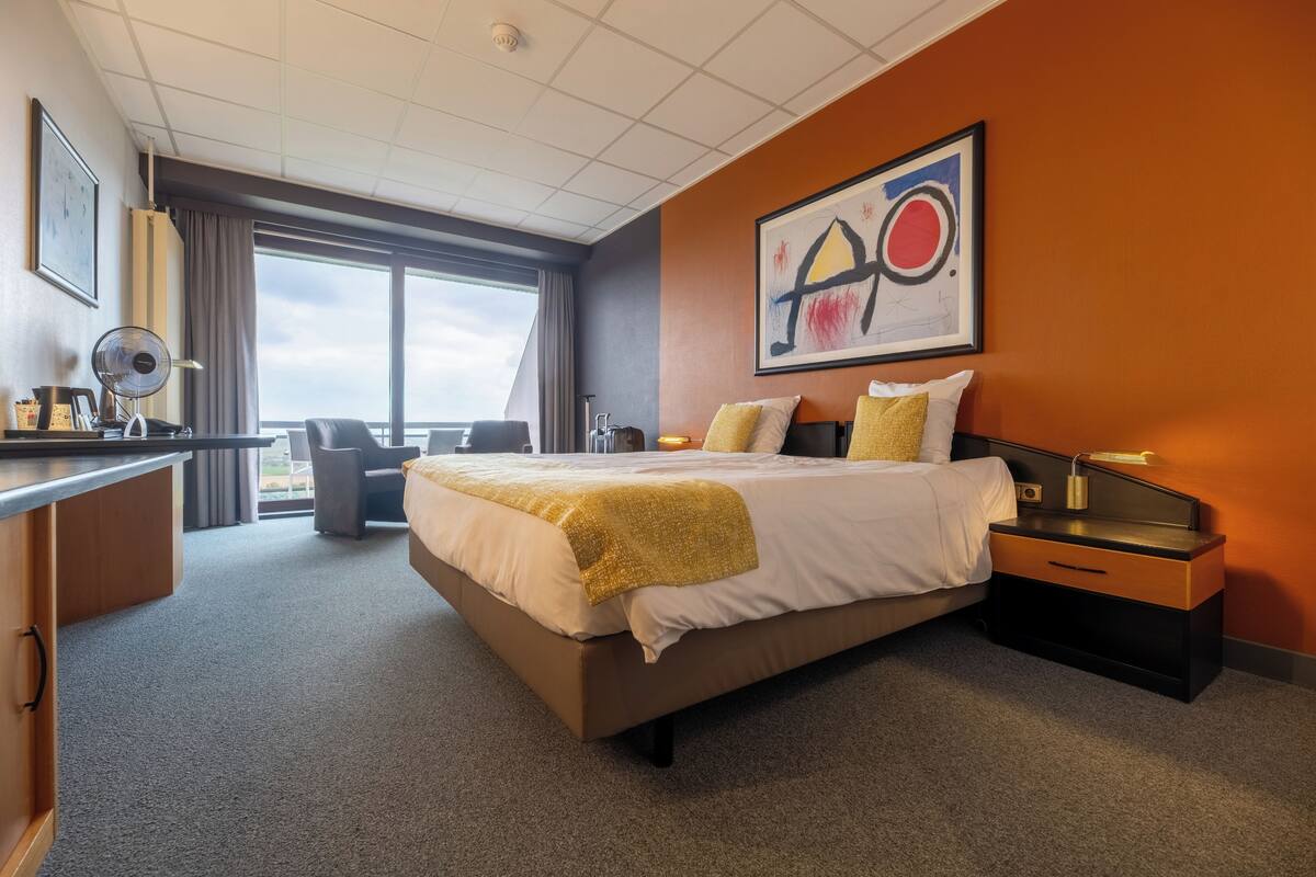 A hotel room with a large bed, a desk, a chair, and a window with a view.