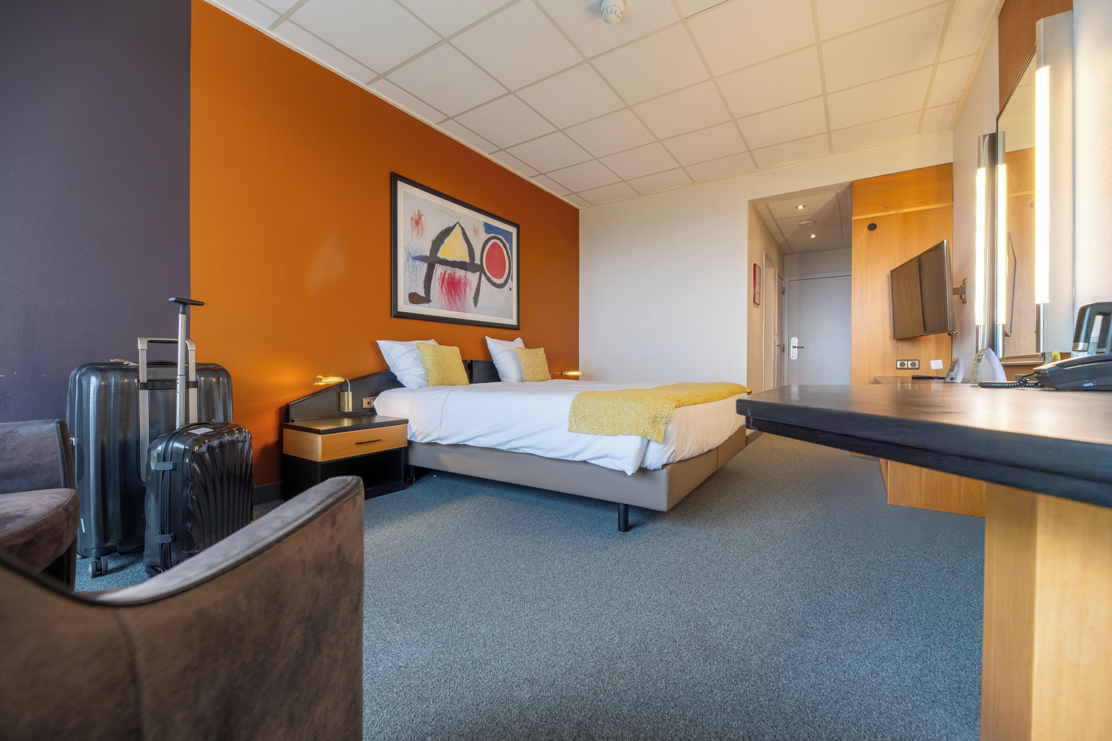 A hotel room with a bed, a desk, a chair, and a suitcase.