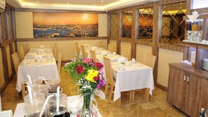A dining area with multiple tables set for service, a large window with a cityscape view, and a buffet station with various food items. - Comfort Elite Hotels Old City (Istanbul)