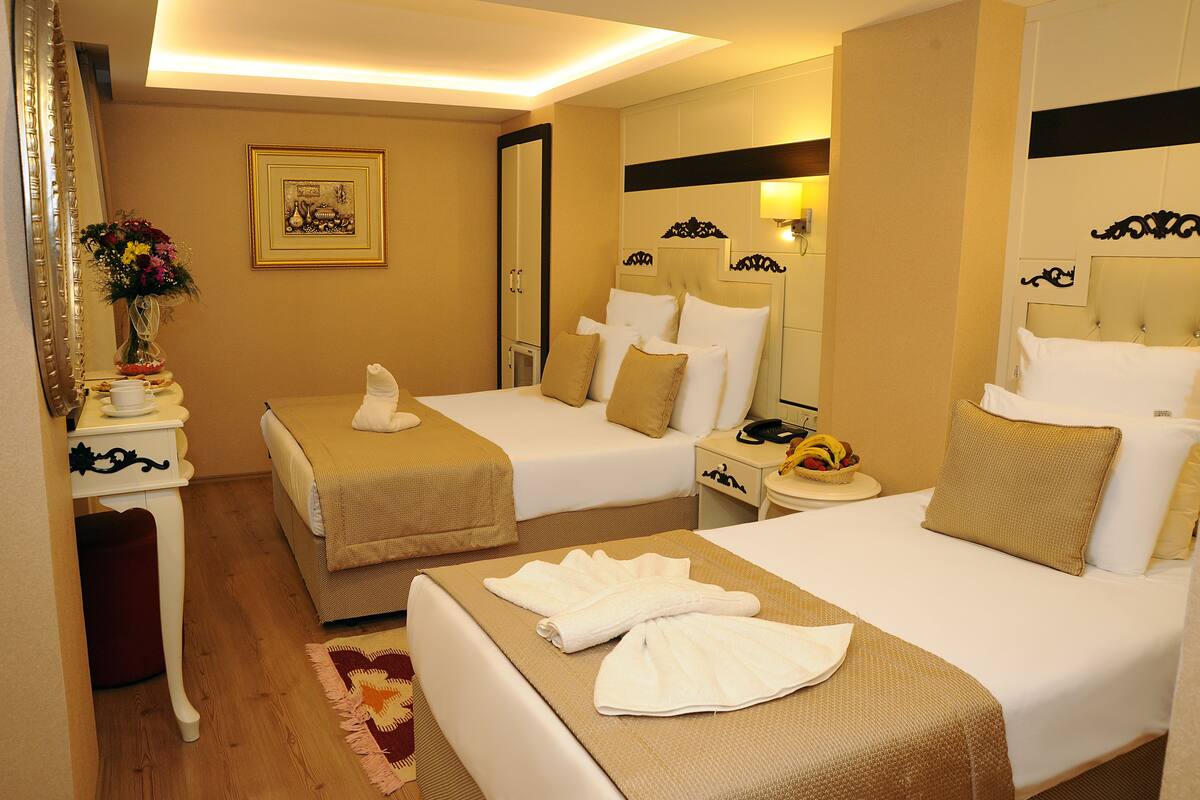 A hotel room with two beds, a bedside table with a lamp, a mirror, and a framed picture on the wall.