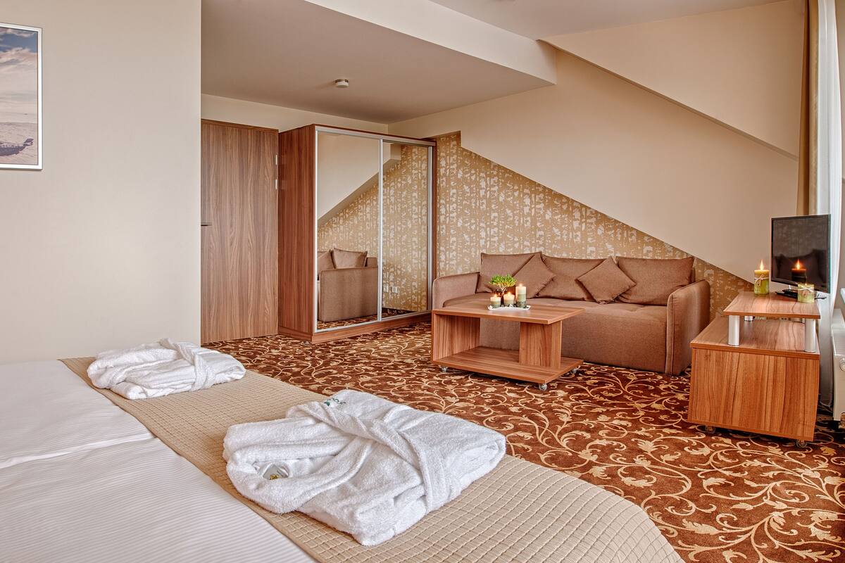A hotel room with two beds, a sofa, a small table with candles, a TV, and a large mirror.