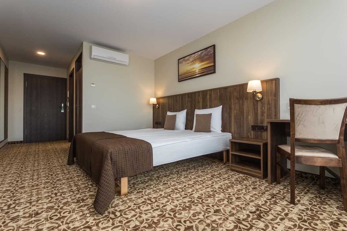 A hotel room with a large bed, a wooden headboard, a chair, and a patterned carpet.