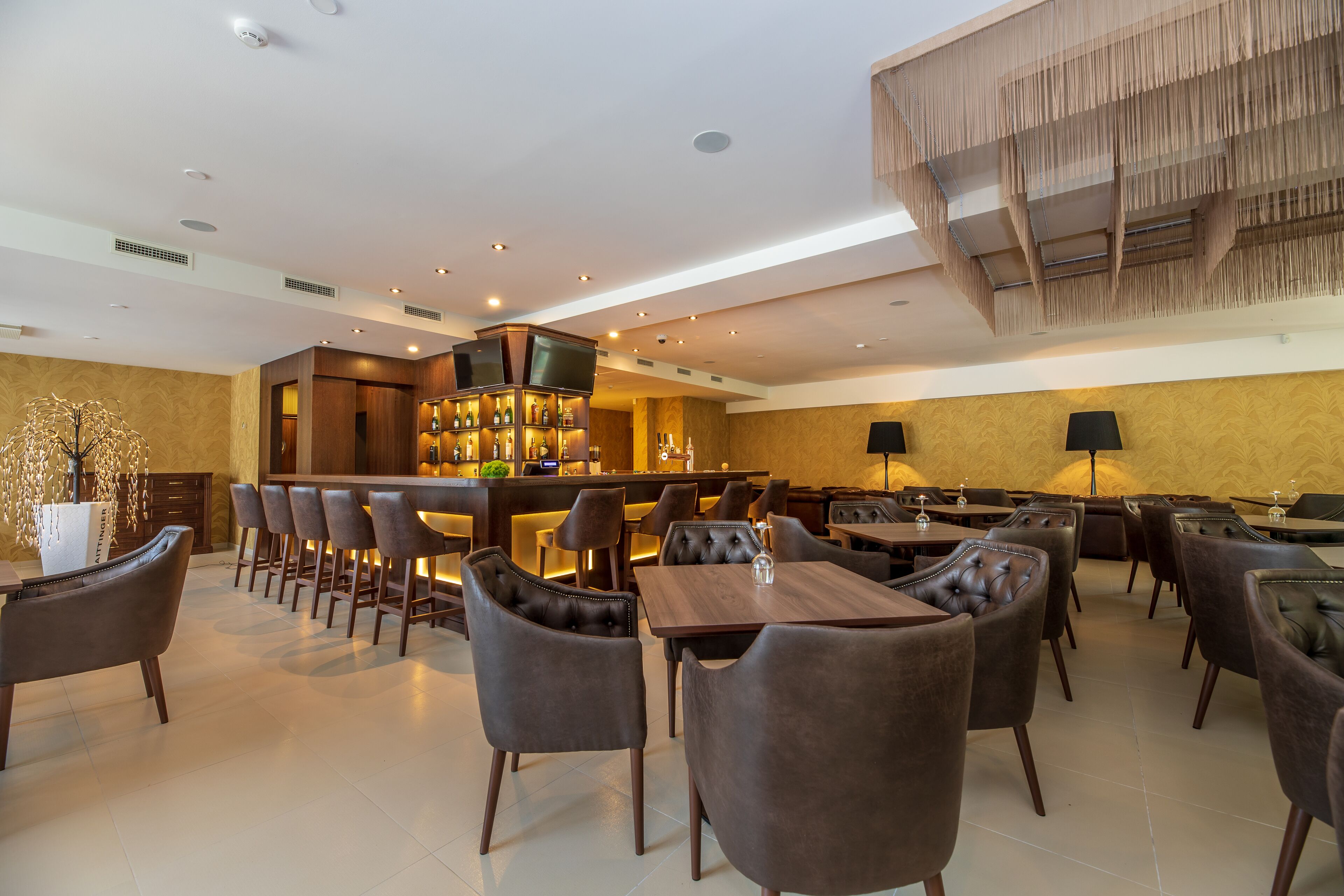 A modern restaurant with a bar area, leather seating, and a decorative ceiling.