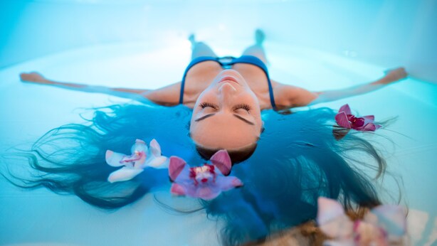 Una persona recostada sobre una superficie, rodeada de agua y flores.