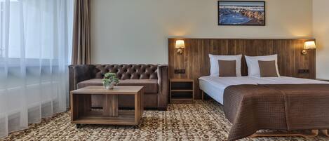 A hotel room with a large bed, a sofa, a small table with a plant, and a painting on the wall.