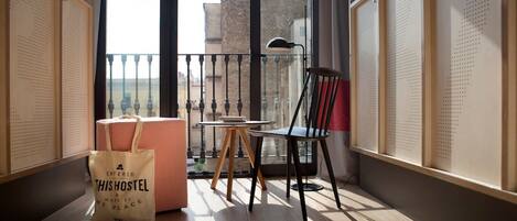 A balcony with a checkered ottoman, a small table, a chair, and a bag labeled "THISHOSTEL".