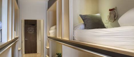 Un pasillo estrecho que conduce a una habitación con cama, cómoda y calefactor en la pared.