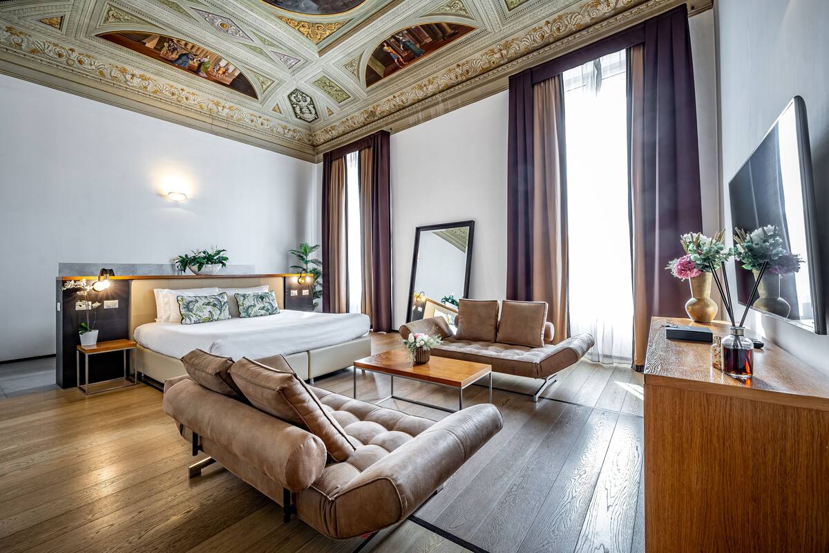 Una camera d'albergo moderna con un letto grande, un divano, un tavolino e una scrivania con uno specchio.