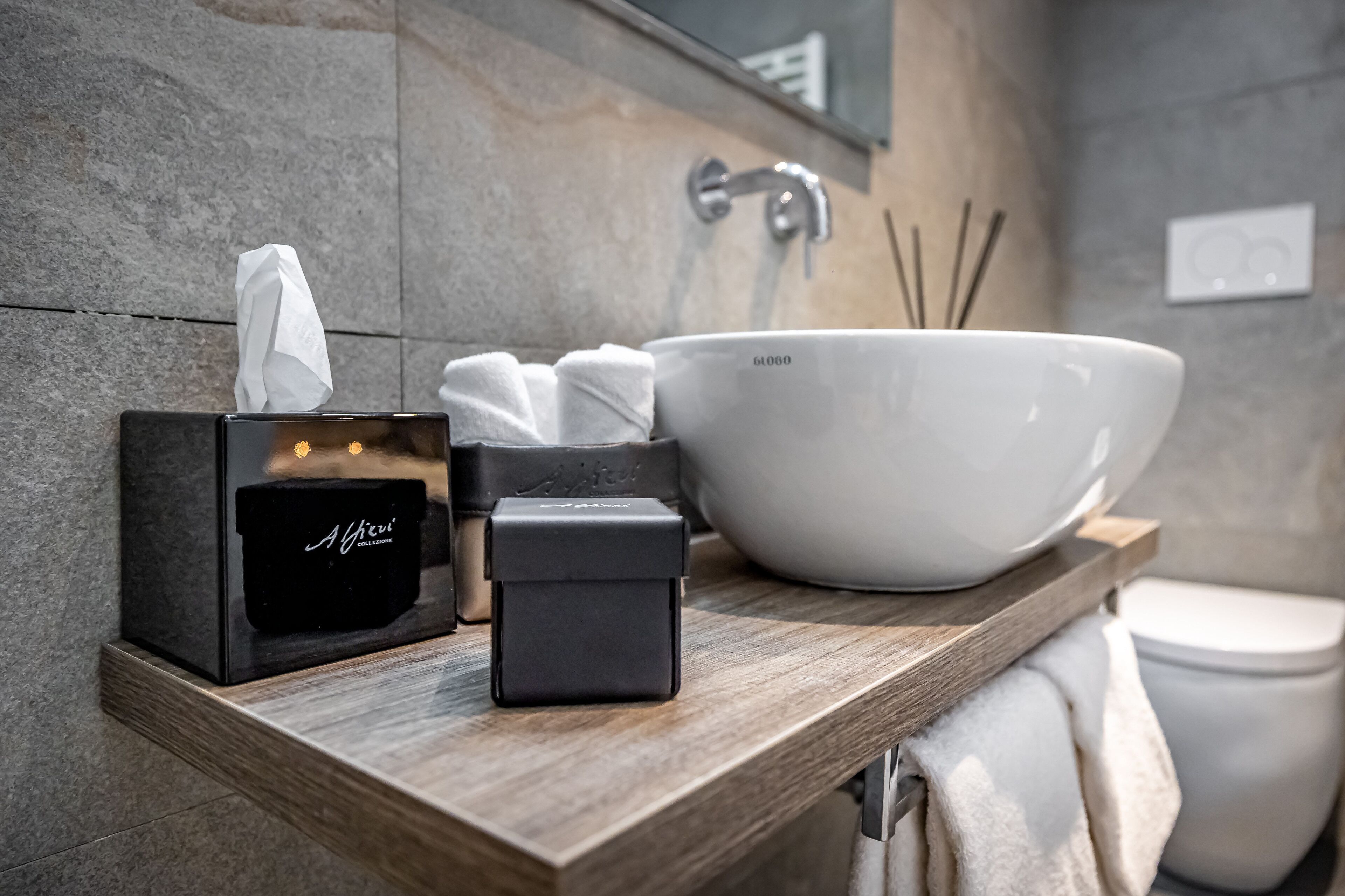 A modern bathroom with a large white sink, a black soap dispenser, a tissue box, and a towel rack.