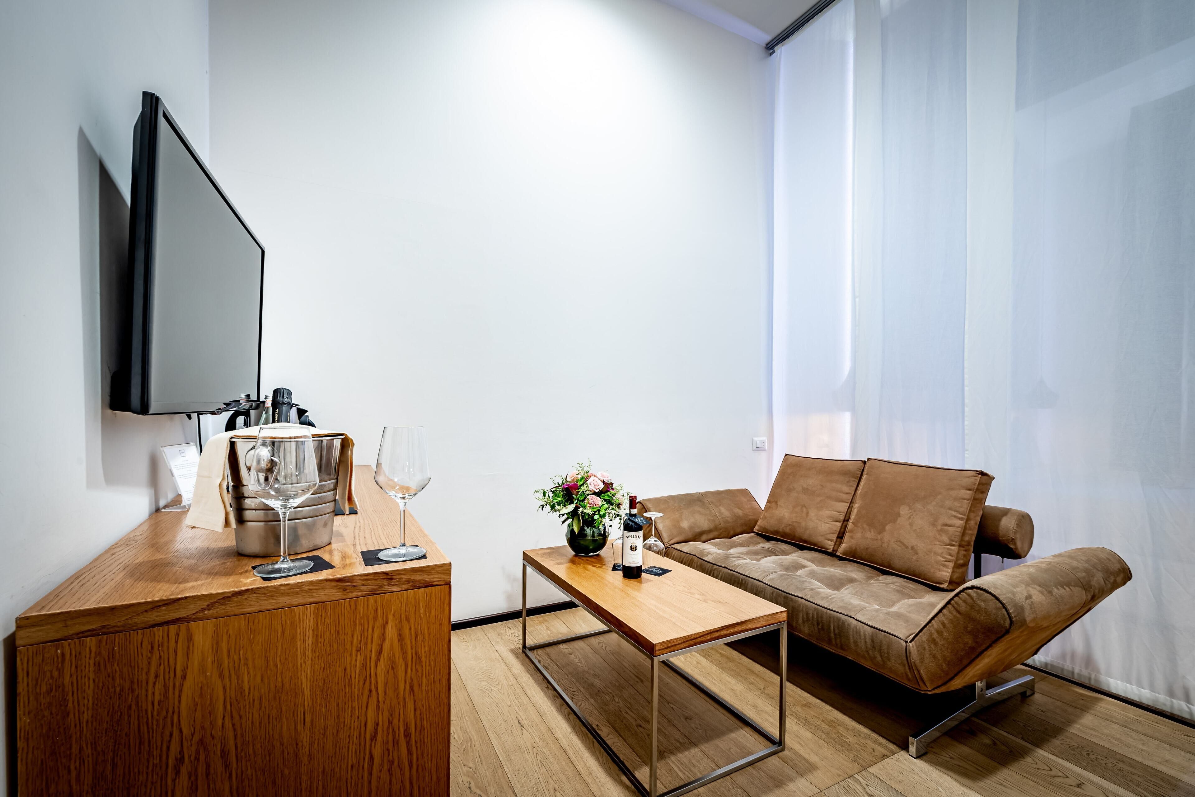 Ein modernes Wohnzimmer mit Couchtisch aus Holz, braunem Sofa, Wand-Fernseher und einem Beistelltisch mit Weinglas und Blumenvase.