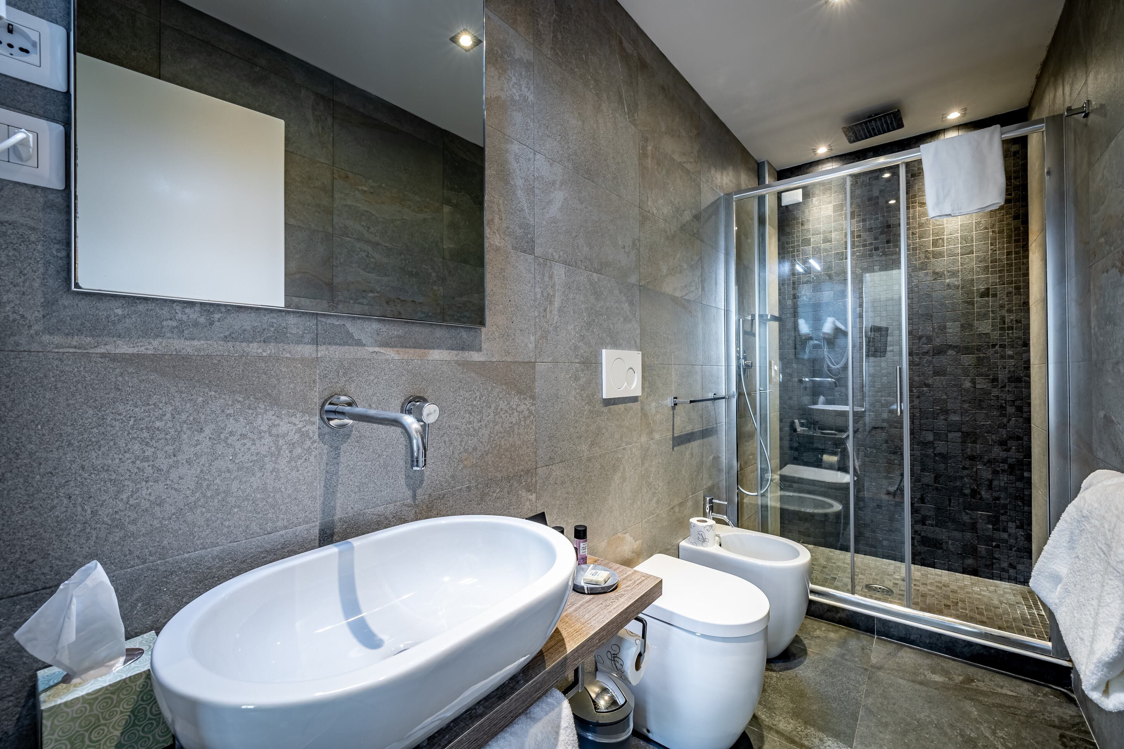 A modern bathroom with a large white sink, a glass shower enclosure, and a mirror above the sink.