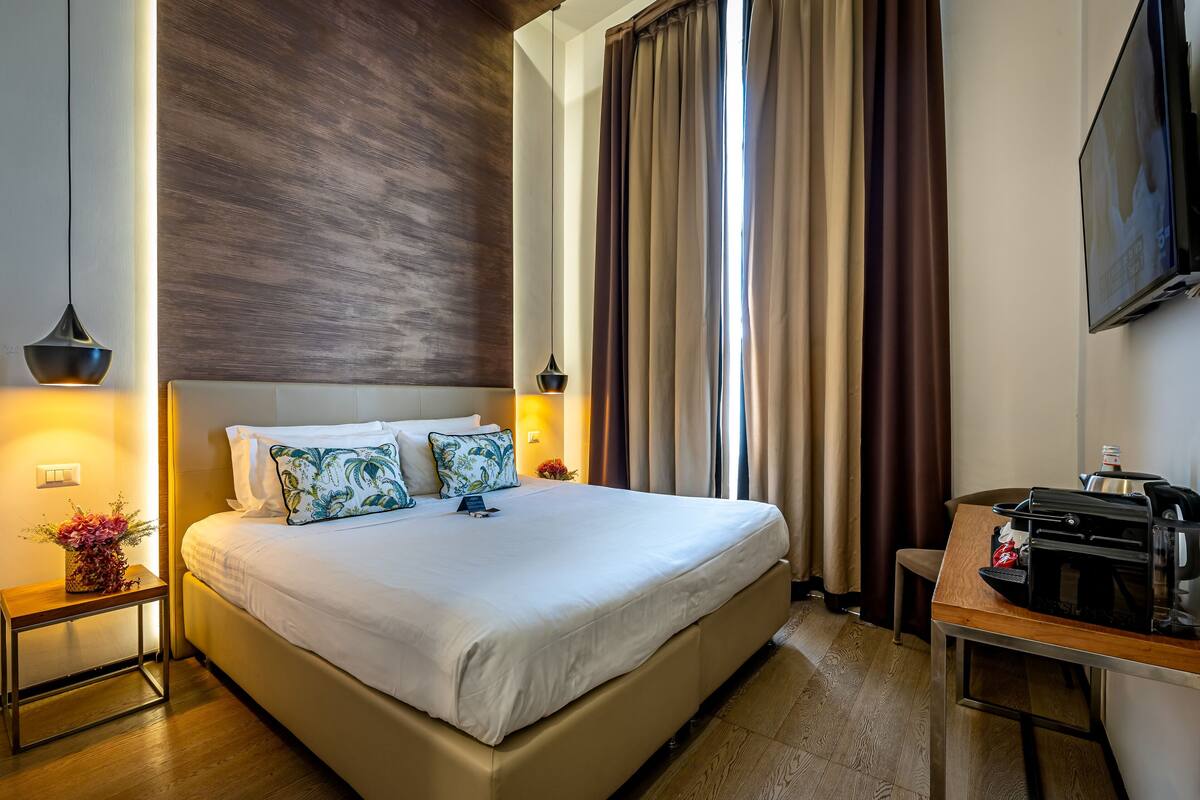 Camera d'albergo con un letto grande, comodini con lampade, una macchina del caffè e un televisore a parete.
