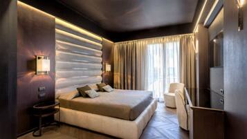 A modern hotel room with a large bed, a sitting area with a chair, and a desk.