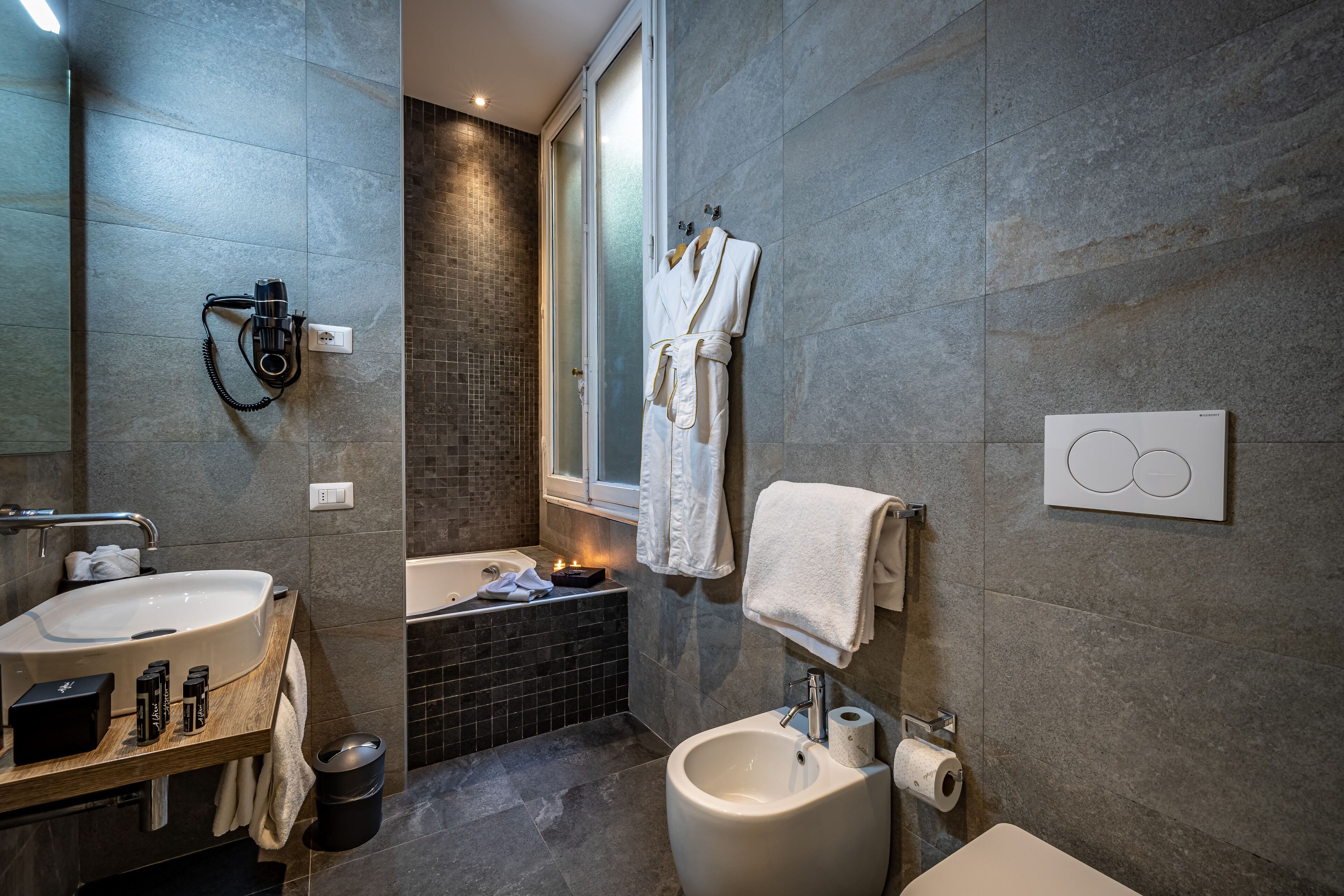 Un baño moderno con un lavamanos grande, un bidé y una bañera. Hay toallas y artículos de aseo en la encimera.