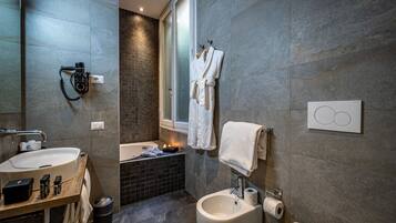 Un baño moderno con un lavamanos grande, un bidé y una bañera. Hay toallas y artículos de aseo en la encimera.