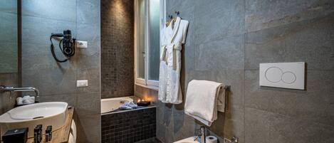 A modern bathroom with a large sink, a bidet, and a bathtub. There are towels and toiletries on the counter.