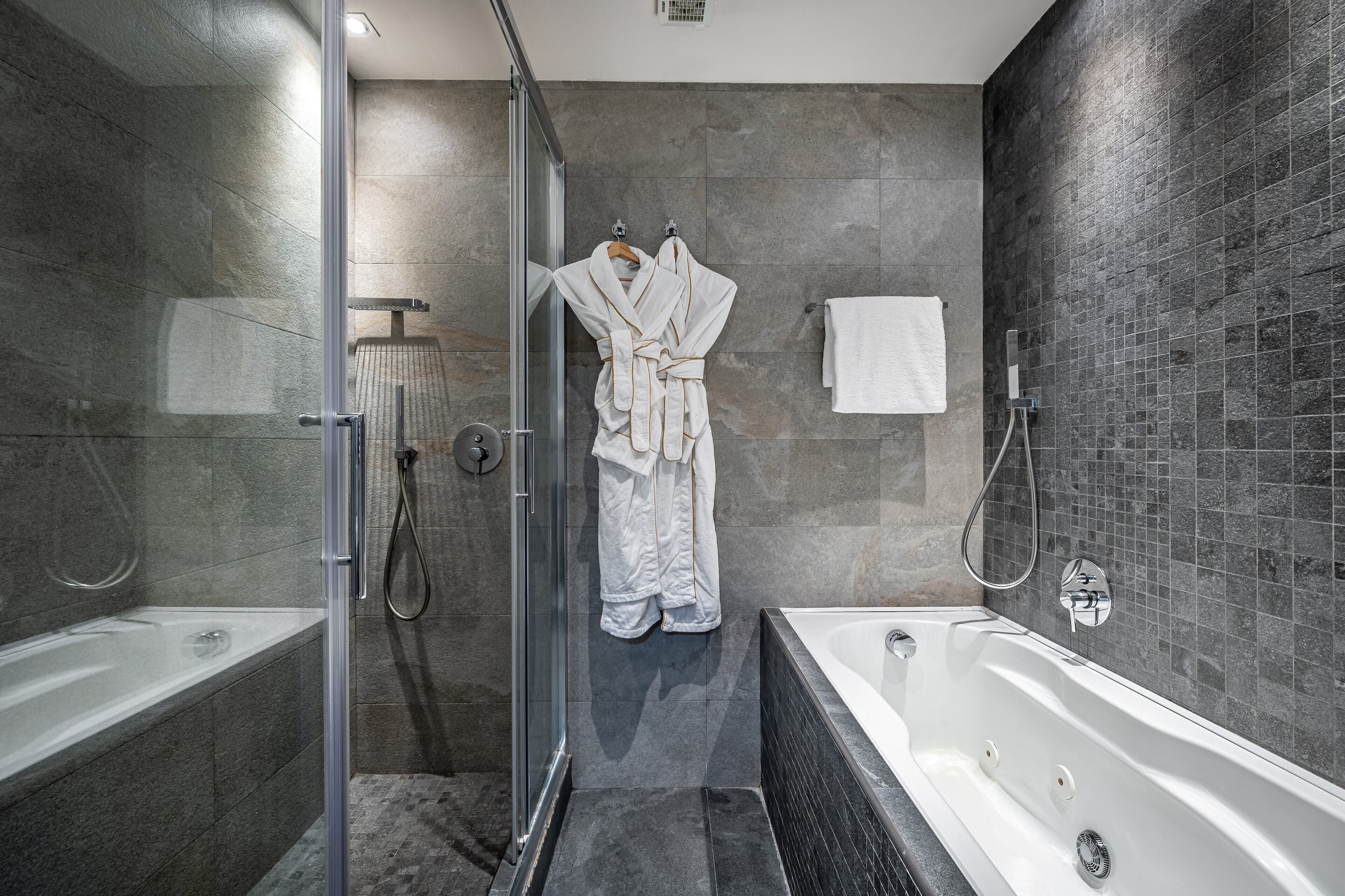 A modern bathroom with a glass-enclosed shower, a separate bathtub, and a towel rack with robes.