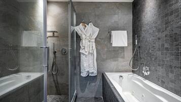 Un baño moderno con ducha de vidrio, bañera independiente y perchero con batas.