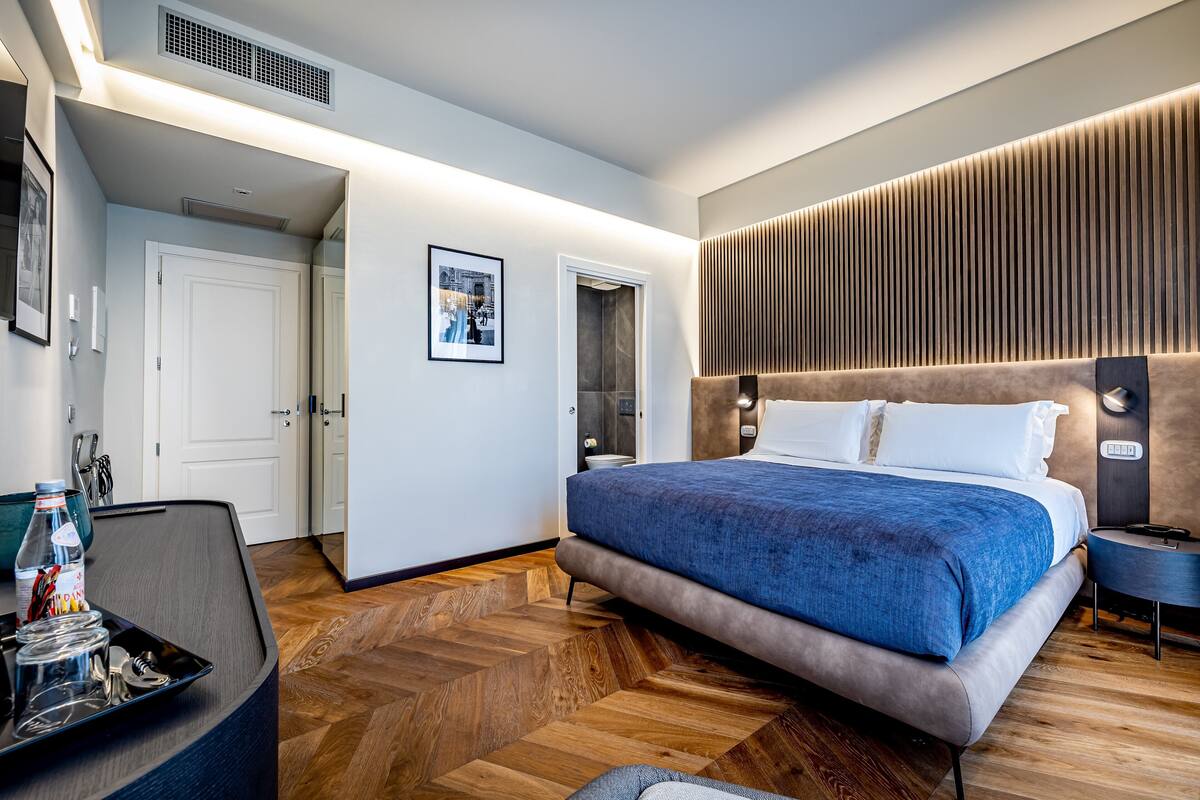 Una camera d'albergo moderna con un letto grande, una scrivania con una sedia, uno specchio e un pavimento in legno.
