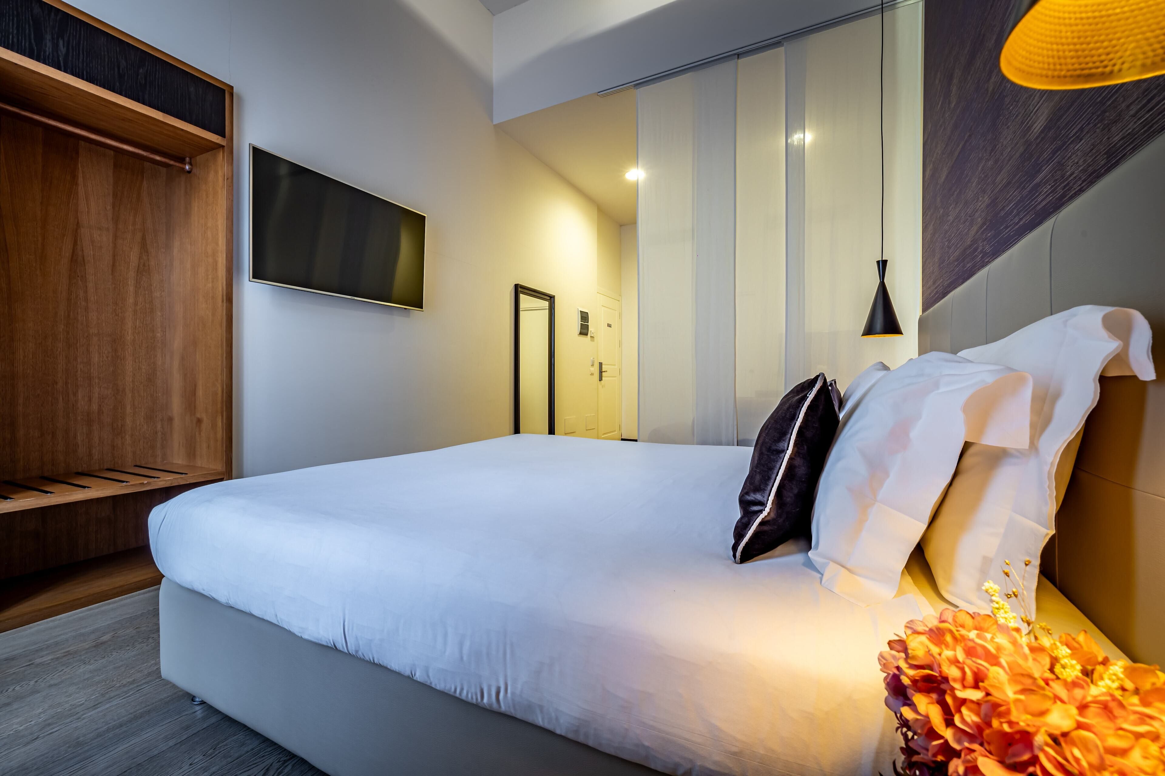 A modern hotel room with a large bed, a wooden wardrobe, a flat-screen TV, and a decorative vase.