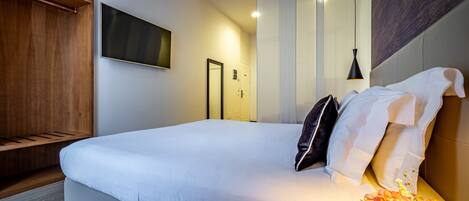 A modern hotel room with a large bed, a wooden wardrobe, a flat-screen TV, and a decorative vase.