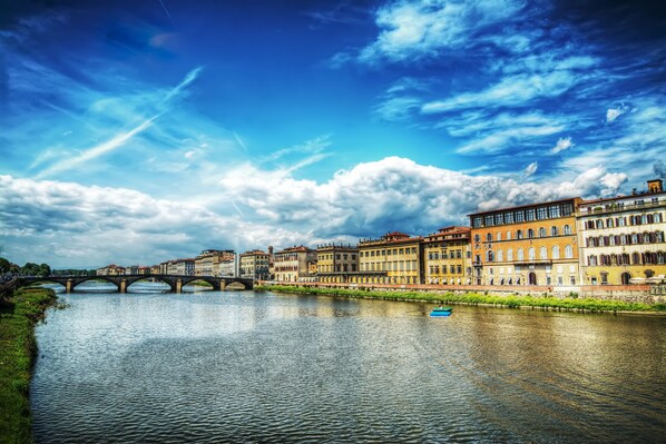 A river with a bridge, historic buildings, and a clear sky. - Palazzo Alfieri Residenza d’epoca  (Florence)