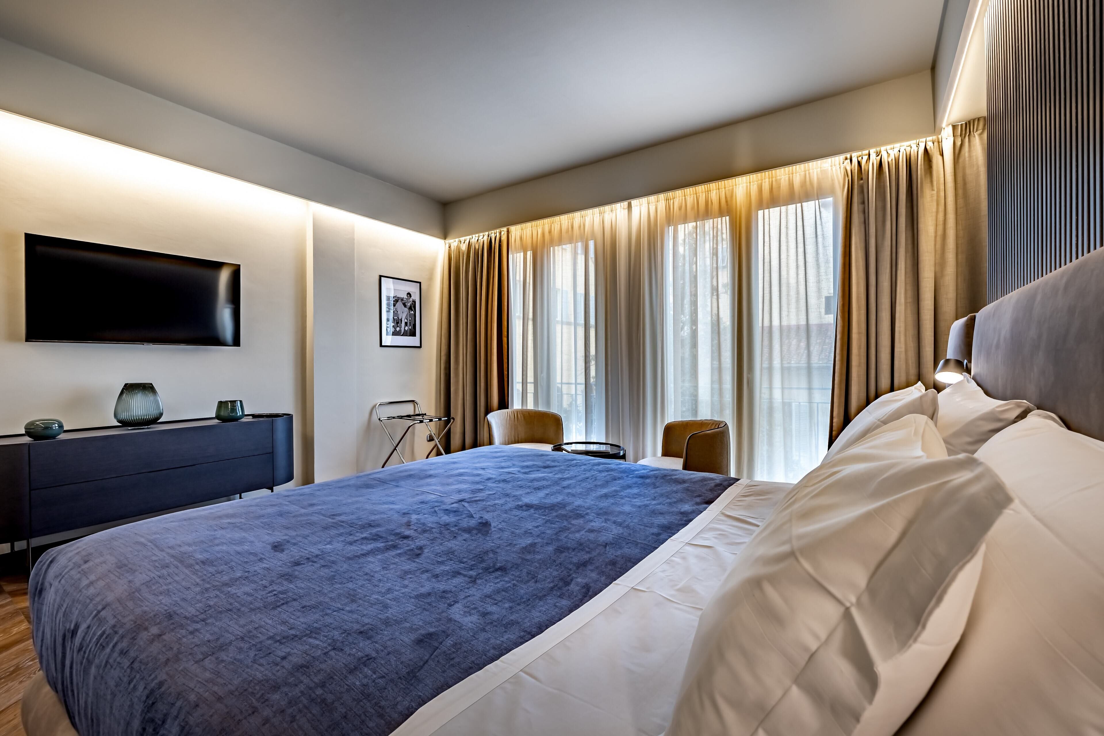 Et moderne hotelværelse med en stor seng, et fladskærms-tv ophængt på væggen, et skrivebord med stol og et vindue med gardiner.