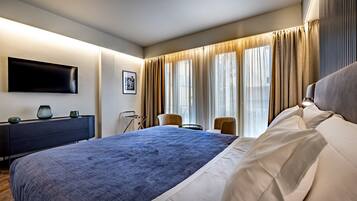 Et moderne hotelværelse med en stor seng, et fladskærms-tv ophængt på væggen, et skrivebord med stol og et vindue med gardiner.